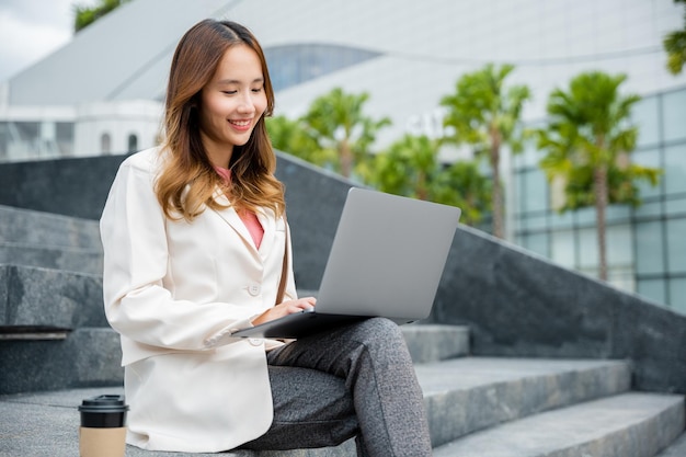 Woman freelance looking laptop with smile while working with coffee cup while sitting on stairs