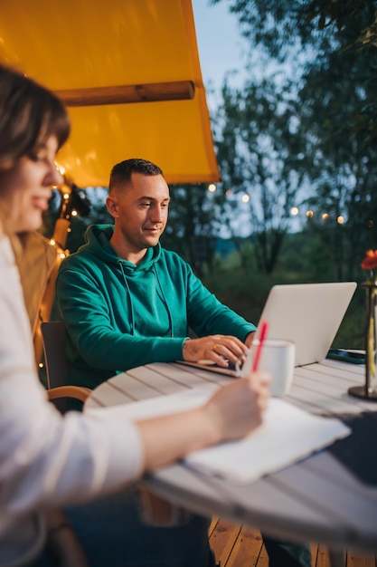 Woman freelancer working laptop and making notes while colleague looking laptop sitting in cozy glamping tent in summer evening Luxury camping tent for outdoor holiday and vacation