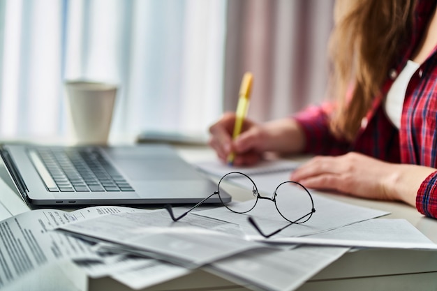 Woman freelancer working remotely on laptop and writing down important data information in notebook.