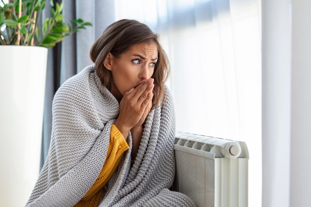 Donna che si congela a casa seduta vicino al radiatore freddo donna con problemi di riscaldamento domestico che sente freddo