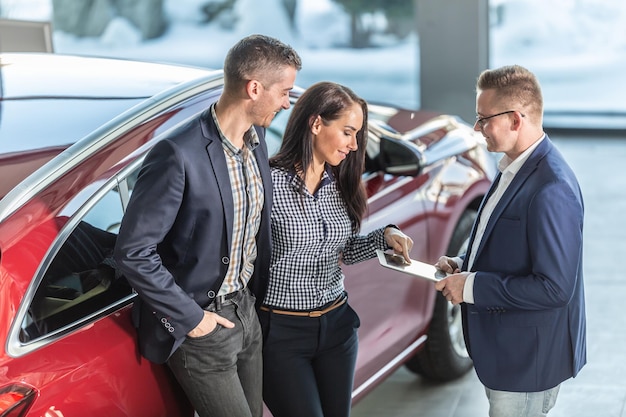 Photo woman from a couple that has decided to buy a car shows details on a tablet to a car dealership employee