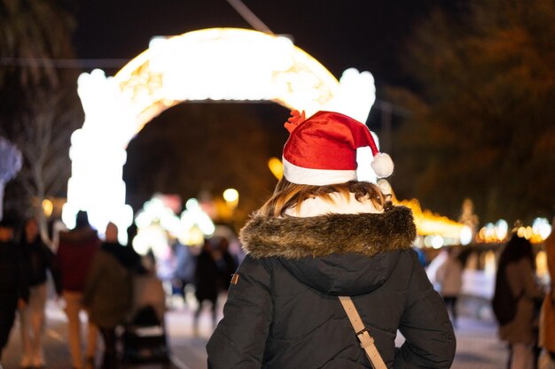 Woman from behind with christmas hat in the night city in winter illuminated door of the market