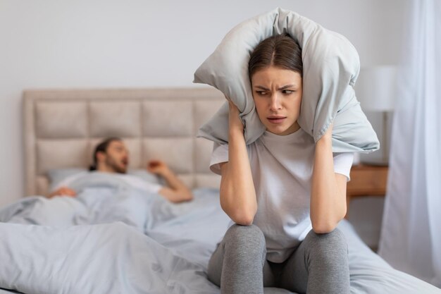 Photo woman frustrated by snoring covering ears with pillow