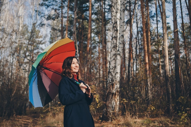 Женщина веселится с красочным зонтиком, гуляет по лесу. Осенний парк. мода, аксессуары, прогулки на свежем воздухе