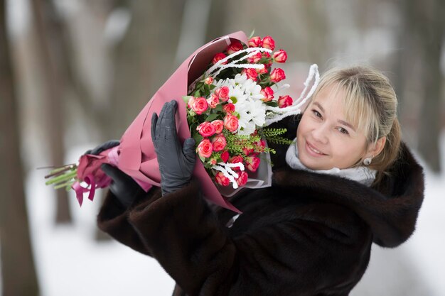 Woman in a fur coat with a bouquet of flowers on a winter background