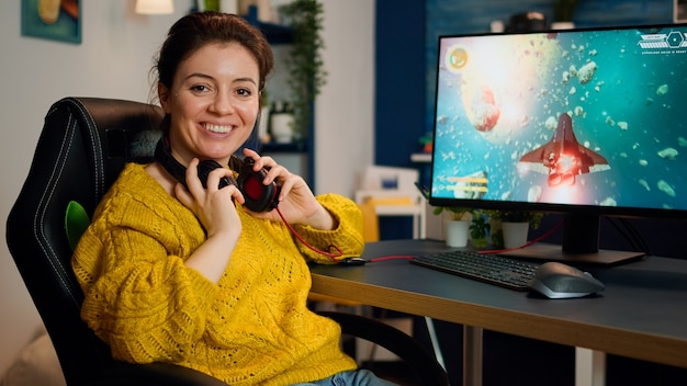 Giocatrice donna che si toglie il sedile guardando la telecamera sorridendo e giocando nel campionato di sparatutto virtuale nel cyberspazio, giocatore di esports che si esibisce sul pc in una stanza elegante durante il torneo di gioco