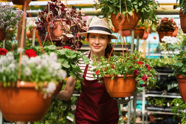 Woman gardener in hat and gloves works with flowers in the greenhouse