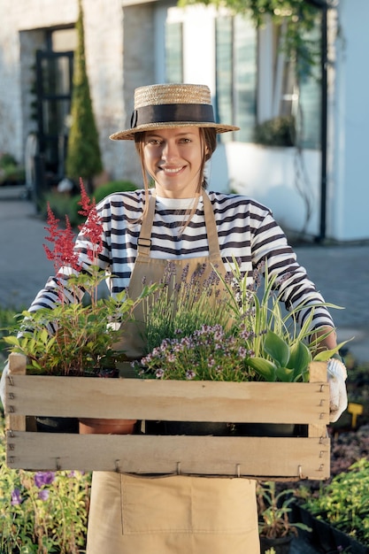 庭で植物でいっぱいの木箱を保持している女性の庭師