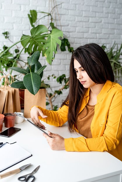 Woman gardener working on digital tablet surrounded with plants