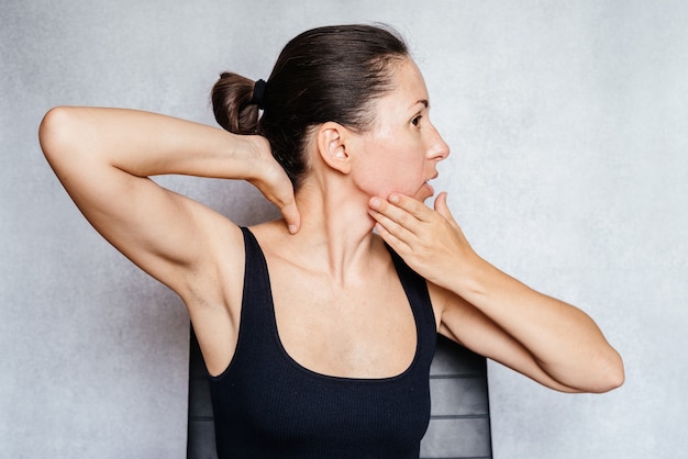 Женщина осторожно вращает головой обеими руками, выполняя упражнения для шеи по методу Маккензи, упражнения для снятия боли в шее.