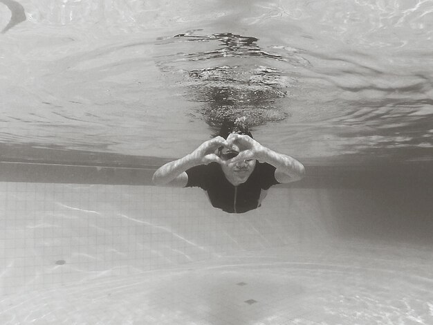 Woman gesturing heart shape while swimming underwater