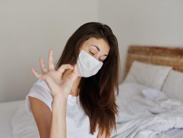 Woman gesturing with hand in medical mask in bedroom