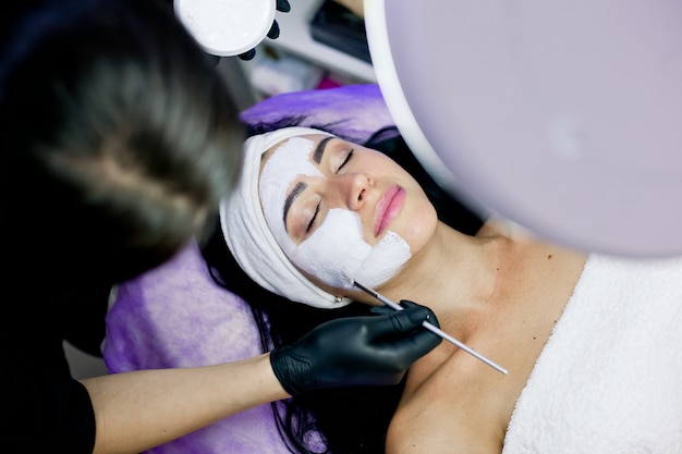 Woman gets face peeling mask, spa treatments, skin care in beauty salon