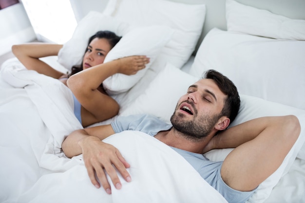 Woman getting disturbed with man snoring on bed in bedroom