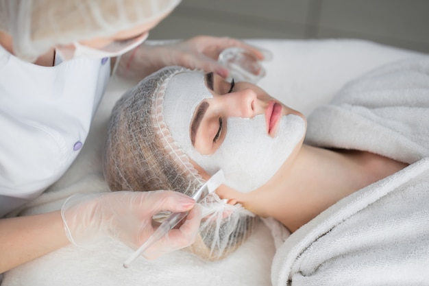woman getting facial care by beautician at spa salon
