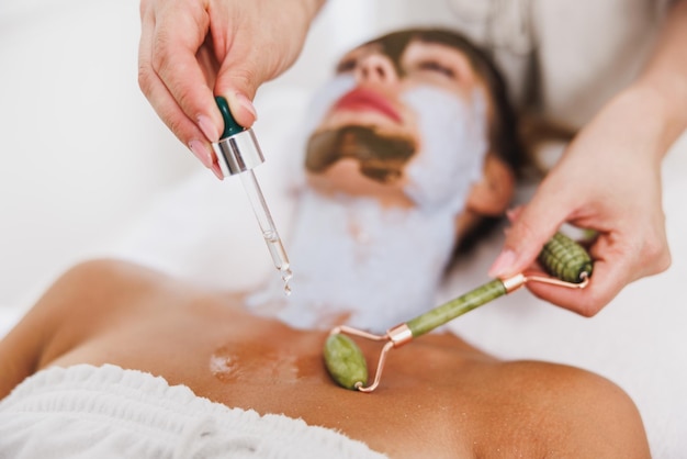 Woman getting a gua sha treatment with a jade roller on decollete zone at the beauty salon.