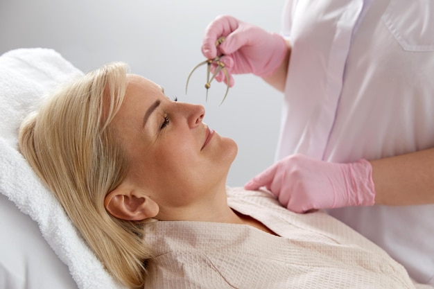 Woman getting her eyebrows angled by a beautician in a beauty salon with instrument