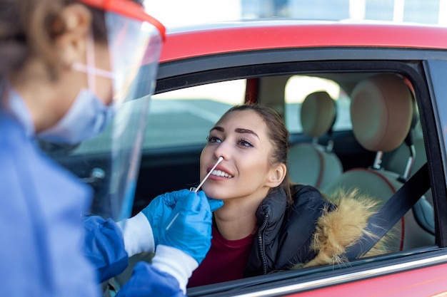 Woman getting tested at a coronavirus drive thru station by medical staff with PPE suit by throat swab Health care drive thru service and medical concept