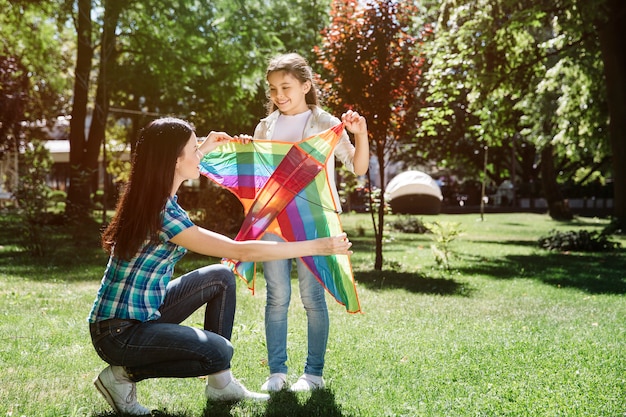 Woman and girl are standing together and holding kite. They are looking at each other and smiling. They are ready to play with kite.