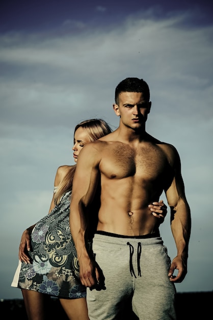 Woman or girl hug bodybuilder man with muscular torso on blue sky couple in love summer vacation rec...