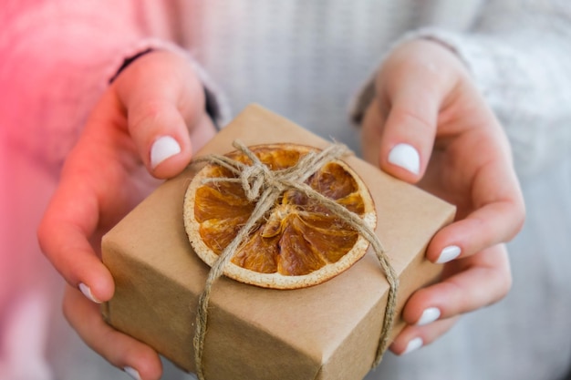 写真 クラフト・ペーパーに包まれ乾燥したオレンジのスライスで飾られた新年のプレゼントを贈る女性の箱