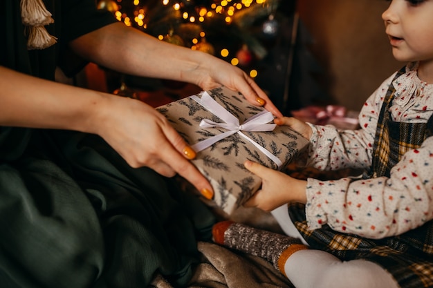 Woman giving a gift to little girl, next to a Christmas tree