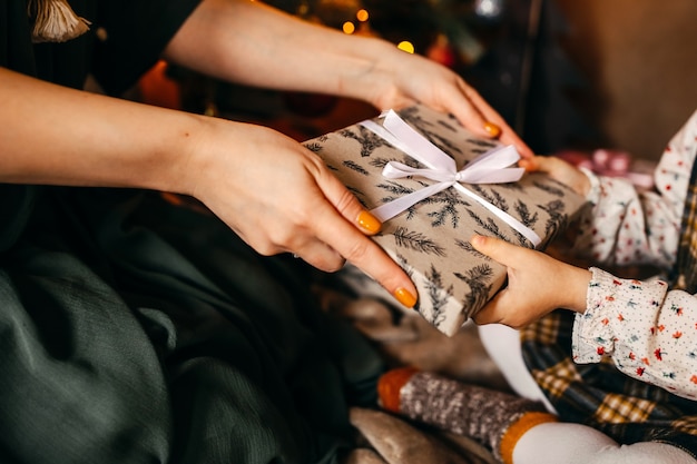 Woman giving a gift to little girl, next to a Christmas tree