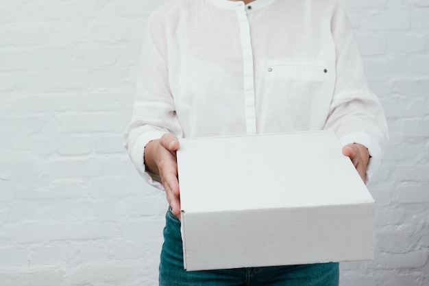 Woman giving parcel on white brick background Woman hands with cardboard box