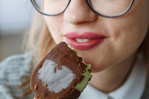 Foto donna con gli occhiali che mangia gelato su un bastone labbra sensuali con cioccolato ghiacciato