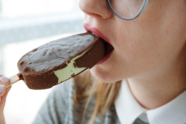 Woman in glasses eating ice cream on stick sensual lips with frost chocolate