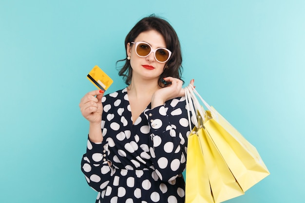 Woman in glasses holding card and bags on the blue background.