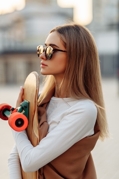 Woman in glasses with a skate in her hands. Longboarding around the city. High quality photo