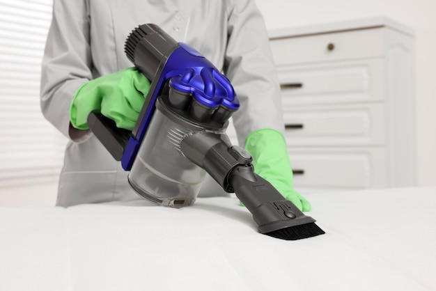 Woman in gloves disinfecting mattress with vacuum cleaner indoors closeup