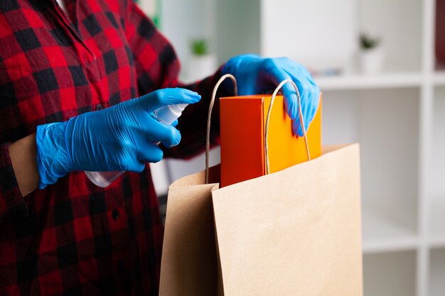 Woman in gloves disinfects product packaging at apartment