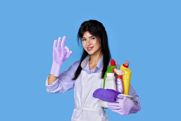 Woman in gloves holding bucket of detergents and showing ok gesture