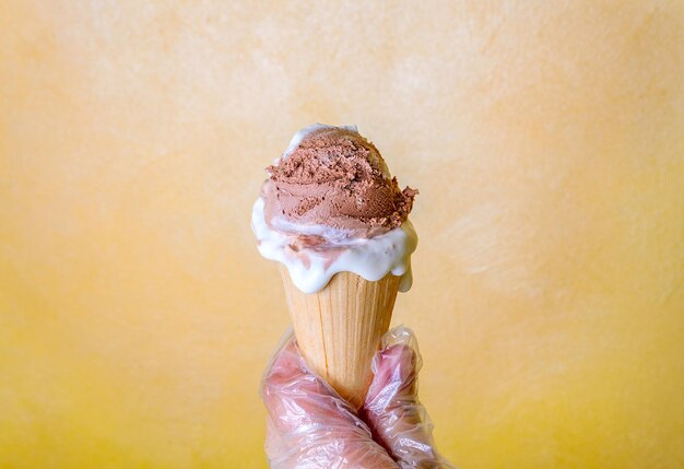 A woman in gloves holds a refreshing chocolate and vanilla ice cream in a waffle cone