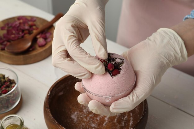 Woman in gloves making bath bomb at white table closeup