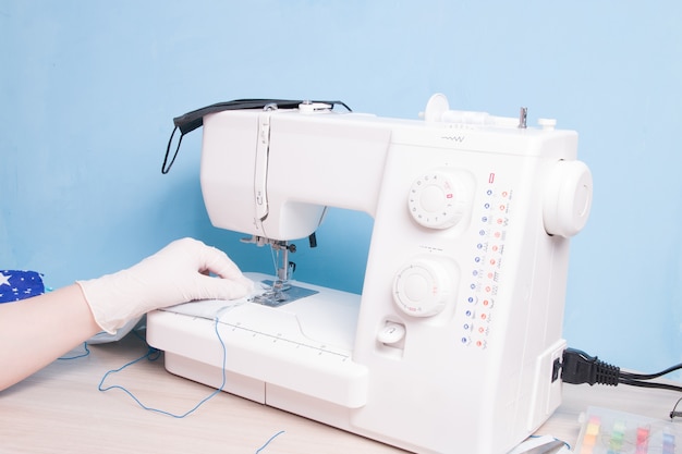 woman in gloves sews a protective face mask on a sewing machine