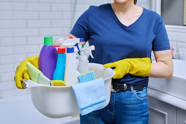 バスルームで洗剤の盆を持った手袋をかぶった女性