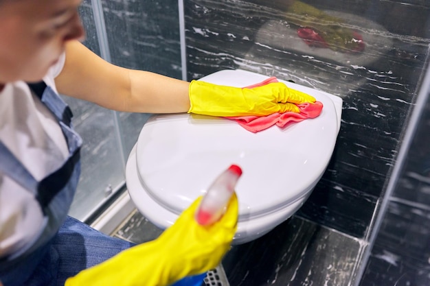 Donna in guanti con detersivo che lava il primo piano della toilette. pulizia, sanificazione e igiene del bagno in casa