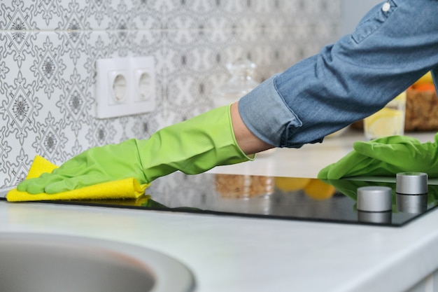 Photo woman in gloves with rag cleaning kitchen, washing electric hob on countertop of kitchen furniture