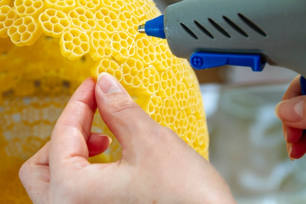 Woman glues pasta with a hot glue gun during the manufacture of crafts
