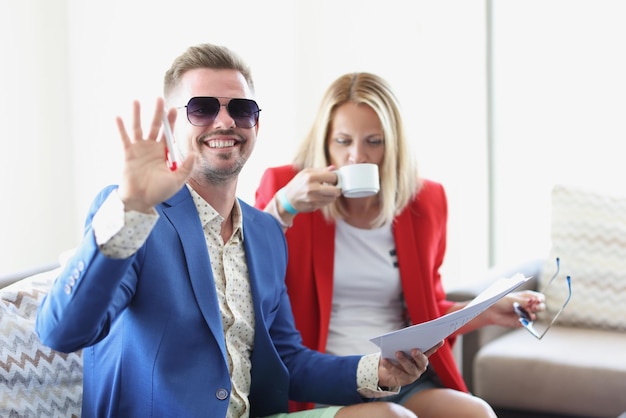 Woman go through business papers and drink coffee man wave hello and smile