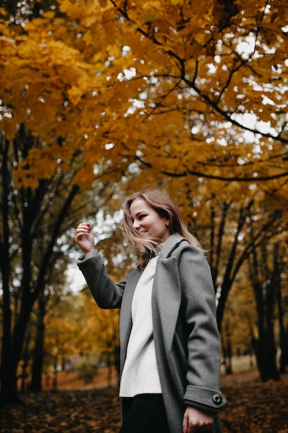 woman goes into along the autumn alley of the park a girl in a gray coat