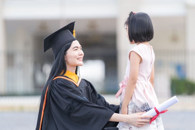 彼女の卒業式の日に小さな女の子と一緒に卒業する女性