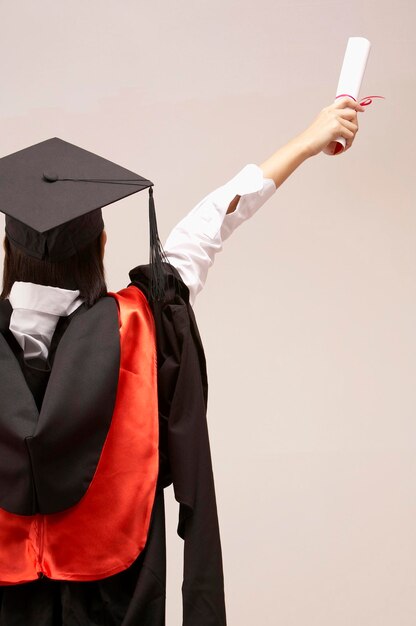 Woman in graduation gown standing against white background