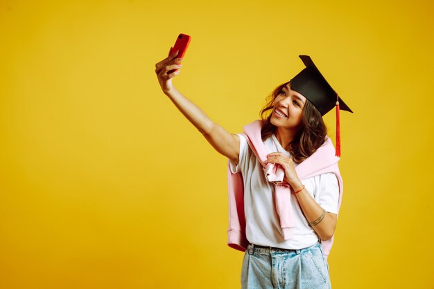 woman in a graduation hat on her head take selfie on yellow