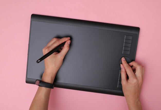 ピンクの背景のグラフィックタブレットで作業する女性のグラフィックデザイナーまたはレタッチャー。上面図