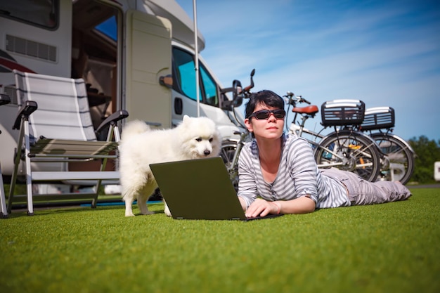 Женщина на траве с собакой, глядя на ноутбук. Автомобиль-караван Отпуск. Семейный отдых, отпуск в автодоме