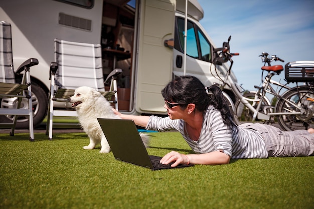 Женщина на траве с собакой смотрит на ноутбук. Отдых на караване. Семейный отдых, отпуск в автодоме